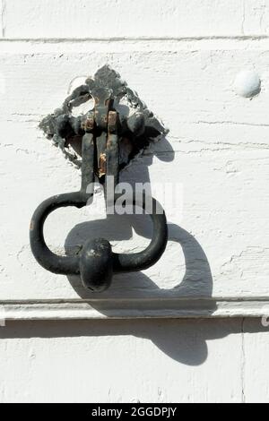 Close-up of an antique door knocker on a weathered white wooden surface showcasing intricate details and unique craftsmanship Stock Photo