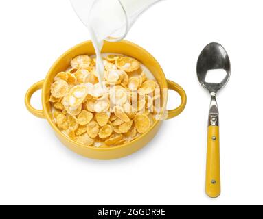 Pouring milk from jug into bowl with tasty cornflakes on white background Stock Photo