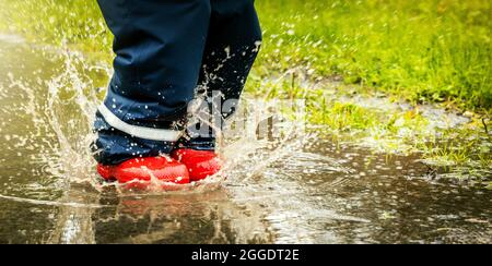 child with red rubber boots jump in puddle on rainy autumn day. waterproof clothing. copy space Stock Photo