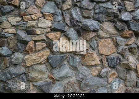 Stone wall texture. Old stone wall with varying sizes , shapes and colored of stones. Stock Photo