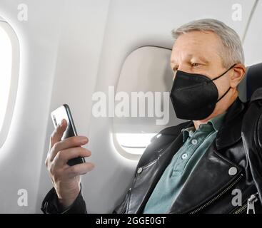 Man wearing face mask and using phone inside airplane during flight. Prevention during Coronavirus COVID-19 pandemic Stock Photo