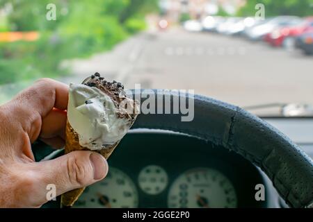 nibbled chocolate and milk cream ice cream in a waffle edible cup in the driver hand inside the car at lunchtime while waiting in hot sunny weather Stock Photo