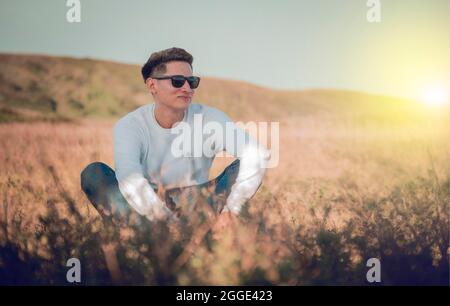 Smiling young man sitting on the grass, smiling young man in eyeglasses sitting on the field, concept of happiness in the field El Crucero, Nicaragua Stock Photo