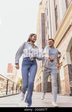 Full-length portrait of young happy couple in motion. Walking around city on warm sunny day Stock Photo