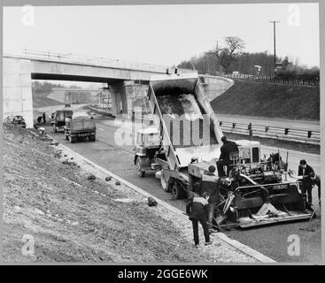 A view of the construction of the Birmingham to Preston Motorway (M6), showing a team of workers surfacing the hard shoulder at Hanchurch. In the background is Structure 340, a bridge on Hanchurch Lane carrying the main water supply into Newcastle-under-Lyme. The bridge shown in the background is located at grid reference SJ8495041600. Stock Photo