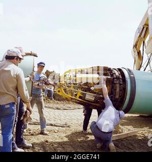 A team of men joining two steel pipes together on the Martin pipeline, showing the internal pneumatic clamp for locking the pipes together. The Martin gas pipeline was installed in 1981 by Laing Industrial Engineering and Construction Ltd for British Gas. Running 84km from Hatton in Lincolnshire to Peterborough, it crossed 50 roads, eight rivers and four railways. Laing's site headquarters was at Martin in Lincolnshire. In the negative register the subject of the photograph reads 'I.E.C. Basildon gas pipe line'. I.E.C. is believed to be a reference to Laing Industrial Engineering and Construct Stock Photo
