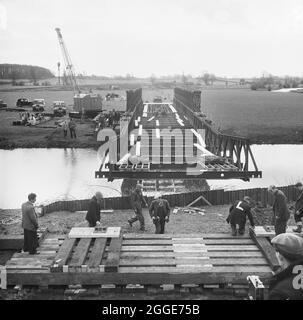 A Bailey bridge being erected across the main channel of the River Great Ouse near Newport Pagnell, during the construction of the London to Yorkshire Motorway (the M1). The caption beneath the corresponding album print states 'The Bailey Bridge being launched is a Double-double, effective span 100'0'', over the Main Ouse channel. 220,000 c/y's of excavated material will be transported over this bridge by Euclids, saving a six mile haul by road. In addition it also makes it possible to travel the full length of B3 Section on the line of the motorway'. Stock Photo