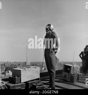 A RAF officer, surrounded by communications equipment, standing on the roof of Coventry Cathedral during the lowering of the 80ft bronze spire. The photograph was taken during 'Operation Rich Man' a joint project involving Royal Air Force staff and Laing staff. This involved a RAF Belvedere helicopter hoisting in to place the 80ft bronze spire on to the new cathedral. The part of the operation to lower the 1/2 ton cross that sits on top of the spire had to be postponed due to windy conditions. Stock Photo