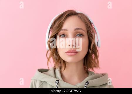 Confident woman listen music headphones Caucasian female enjoy podcast or audio books dressed oversize hoodie pink background close up portrait Stock Photo