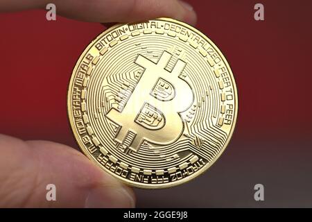 Deutschland. 29th Aug, 2021. Bitcoin coin held between two fingers against a neutral, red background. Symbolic photo for the cryptocurrency.     For editorial use only     Only for editorial use     || Model released Credit: dpa/Alamy Live News Stock Photo