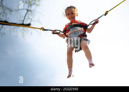 Child jumping child trampoline rubber bands Amusement park Little girl jump on attraction Stock Photo