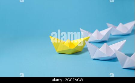 Leadership business concept with a yellow leader paper boat leading among white ones on blue background with copy space. Stock Photo