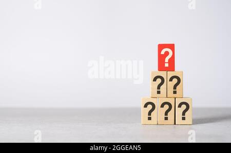 Main question concept with a question mark printed on a red wooden block on top of others black questions with copy space on light grey background. Stock Photo