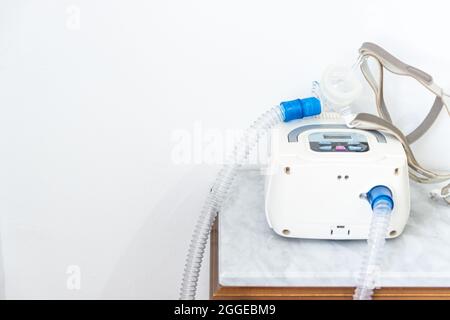 CPAP machine with air hose and head mask on bedside table Stock Photo