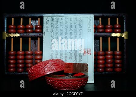Carved old vermilion lacquer box with Chinese name stamp, in the background an abacus, studio shot in front of black background Stock Photo