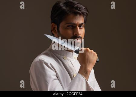A CHEF POSING IN FRONT OF CAMERA IN SERIOUSNESS WITH KNIFE IN HAND Stock Photo
