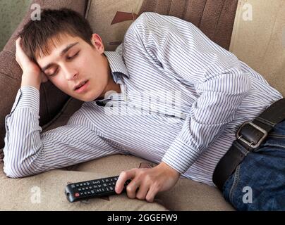 Tired Young Man sleep with TV Remote Control on the Sofa at the Home Stock Photo