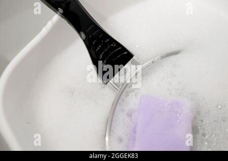 frying pan in soapy washing up water in white plastic bowl Stock Photo