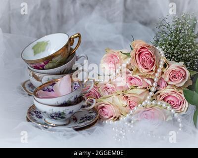Shabby chic bridal still life arrangement with pink flowers, vintage tea cups and pearls. Stock Photo