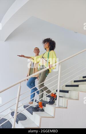 African-American dressmaker points on something in front to mature colleague going down on steps Stock Photo