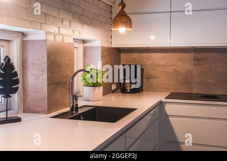 Modern kitchenette with white worktop, black sink and metal lamps, industrial style Stock Photo