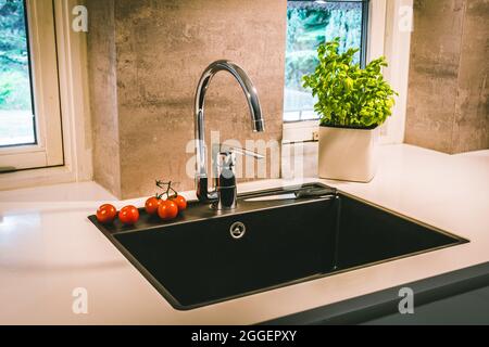 Black sink with chrome fittings in a white worktop in a modern kitchen Stock Photo