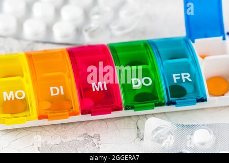 Colorful pill box for weekly dosing on white background, abbreviations for days of the week in German, close-up Stock Photo