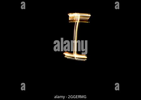 Letter I. Light painting alphabet. Long exposure photography. Drawn letter I with gold lights against black background. Stock Photo