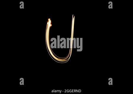 Letter U. Light painting alphabet. Long exposure photography. Drawn letter U with gold lights against black background. Stock Photo
