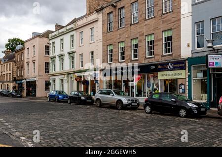 On a grey autumn afternoon cars are parked along the cobblestone road in front of the many shops in the centre of historic Kelso Stock Photo