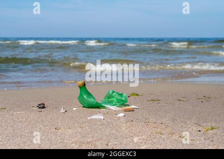Pollution of the coast with plastic bottles. Garbage on the beach. Plastic on the beach. Green empty bottle. Stock Photo