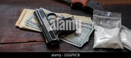 Drugs narcotics illegal business concept. Cocaine plastic packets, pistol and US dollars banknotes on a table. White powder addiction and crime Stock Photo