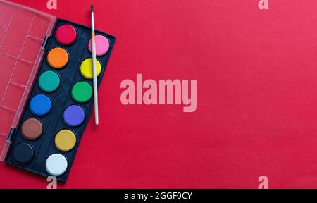 Creative kids, painting and drawing. Colorful paints and brush on red color background, empty space, template. Education, Back to School concept. Stock Photo