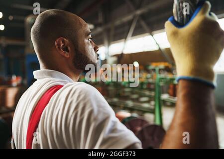 Engineer in uniform using crane controller hanging from ceiling in a factory Stock Photo