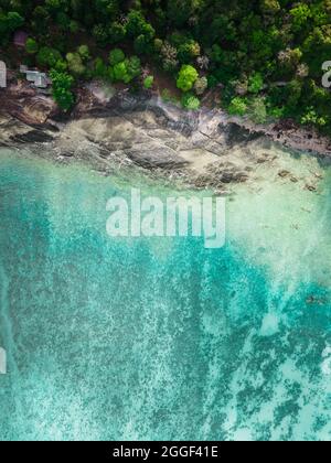 Looking directly down with a drone shot over clear tropical waters on the island of Phi Phi in Thailand with rocks, trees and turquoise waters. Stock Photo
