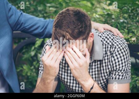 Guys Sharing Life Problems Always Support Best Friends. Friends Getting Down Heart Broken. Sad Man sitting outdoor in the park feeling sadness has a p Stock Photo