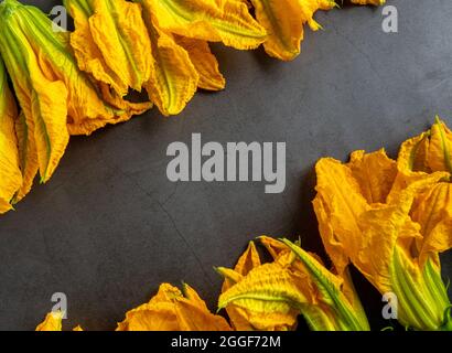 zucchini flowers are arranged in two rows facing each other on a black stone background. Stock Photo