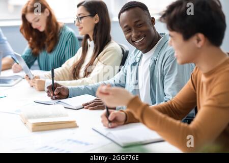 Friendship, Education And Teamwork Concept. Smiling international students sitting at table in public library and talking, doing homework together aft Stock Photo