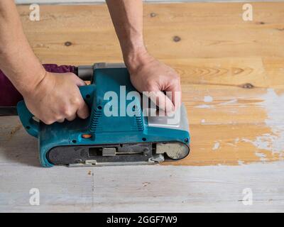 Closeup of caucasian male hands operating a belt sander in order to remove white paint from a wooden floor. Stock Photo