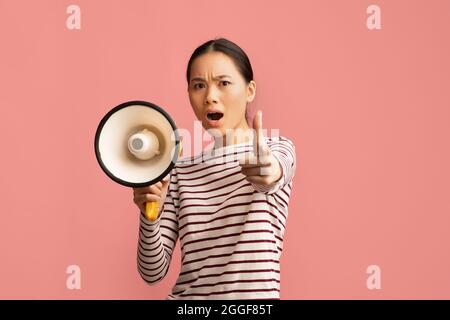 Attention. Emotional Asian Lady With MLoudspeaker In Hand Shouting And Pointing Finger At Camera, Agressive Korean Woman Screaming With Megaphone, Mak Stock Photo