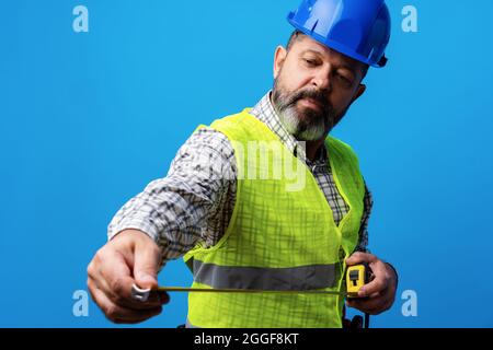 Male builder holding measuring roulette against blue background Stock Photo
