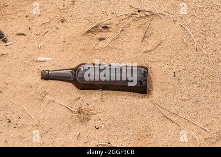Someone left an empty bottle on the sand instead of recycled it. Stock Photo