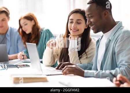 Education And Teamwork Concept. Smiling international female and male students sitting at desk in public library and talking, doing homework or group Stock Photo