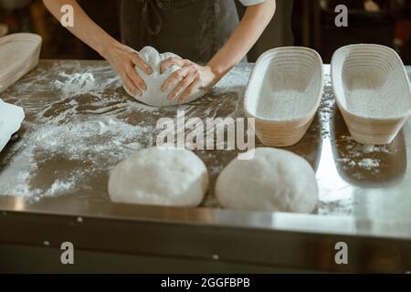 Lady kneads piece of raw dough at metal table in contemporary shop Stock Photo