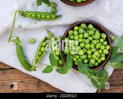 Fresh green peas in a ceramic bowl, pods, on an old wooden surface Stock Photo
