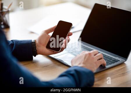 Unrecognizable Arab businessman using laptop and cellphone with mockups for website or app design, cropped. Closeup of male freelancer working with ga Stock Photo