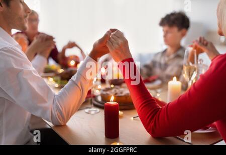 Closeup view of multi generation family holding hands and praying before festive family dinner, celebrating Thanksgiving or Christmas, expressing than Stock Photo