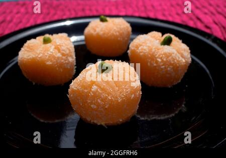 Delicious Orange coconut laddu sweets for festivals like Ganesh chaturthi. Coconut burfi with Orange shape and garnished with pista Stock Photo