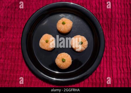 Delicious Orange coconut laddu sweets for festivals like Ganesh chaturthi. Coconut burfi with Orange shape and garnished with pista on black plate wit Stock Photo