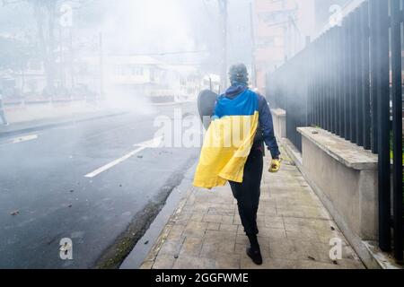 A protester wrapped in the Colombian flag walks down a street amidst a smog of teargas during a protest in Popayan.Protesters confront police in protest of the assassination of Esteban Mosquera, a student leader and anti-police brutality activist in Popayán. The protest is part of an on-going national strike that began in Colombia on April 28th in reaction to tax reforms that would target the poorest in the country.